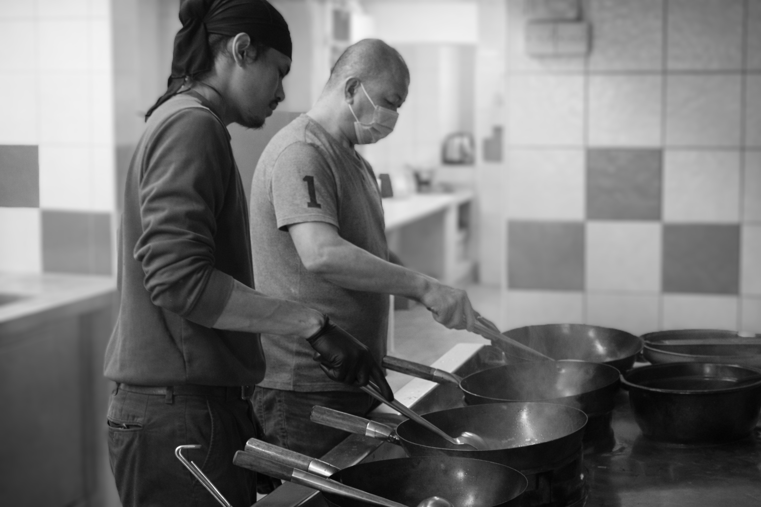 Two chefs working side by side at the woks